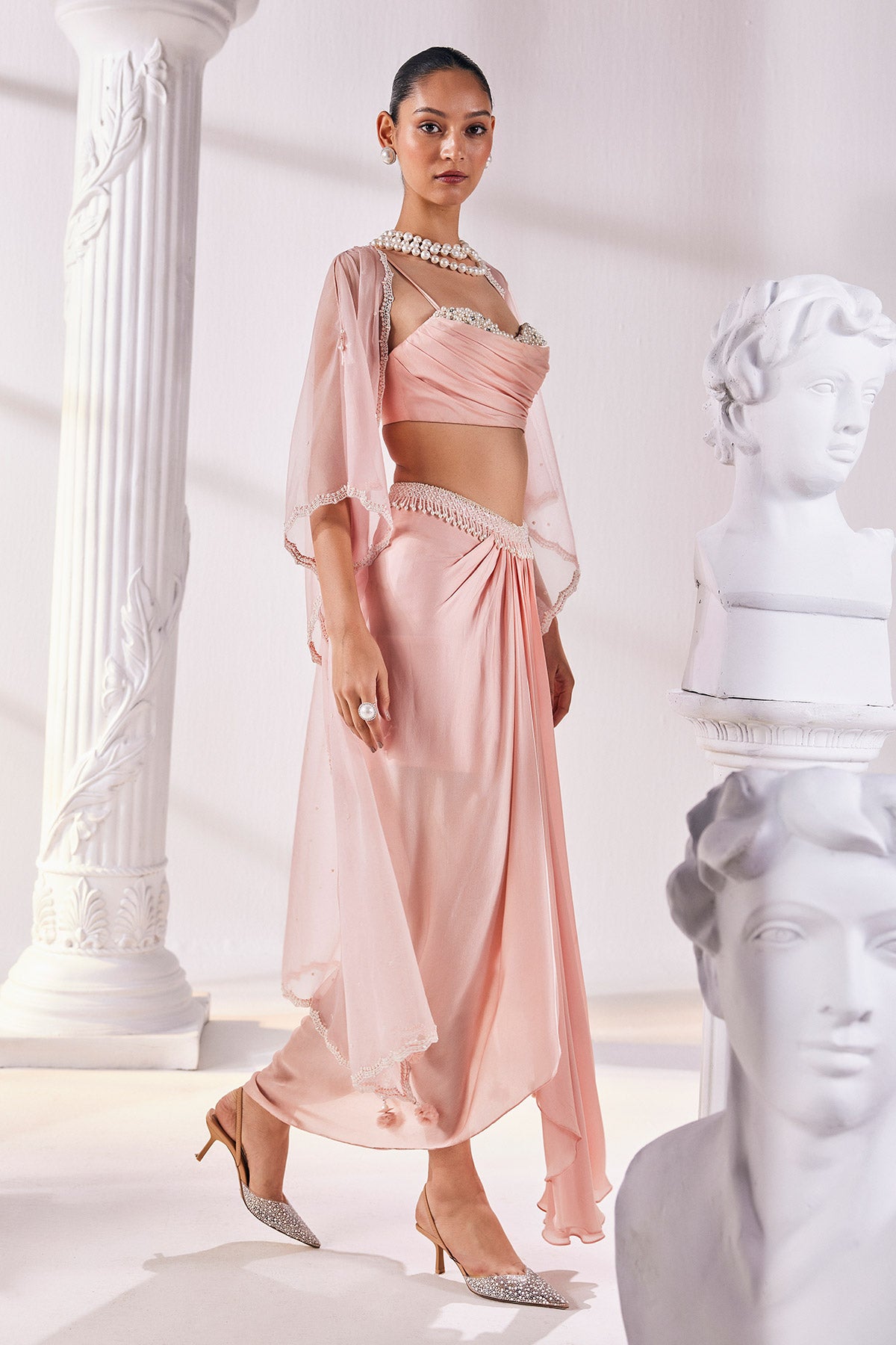 Peach Draped Skirt In Satin Georgette Paired With A Belt And A Pearl Detailed Blouse With A Soft Organza Cape.