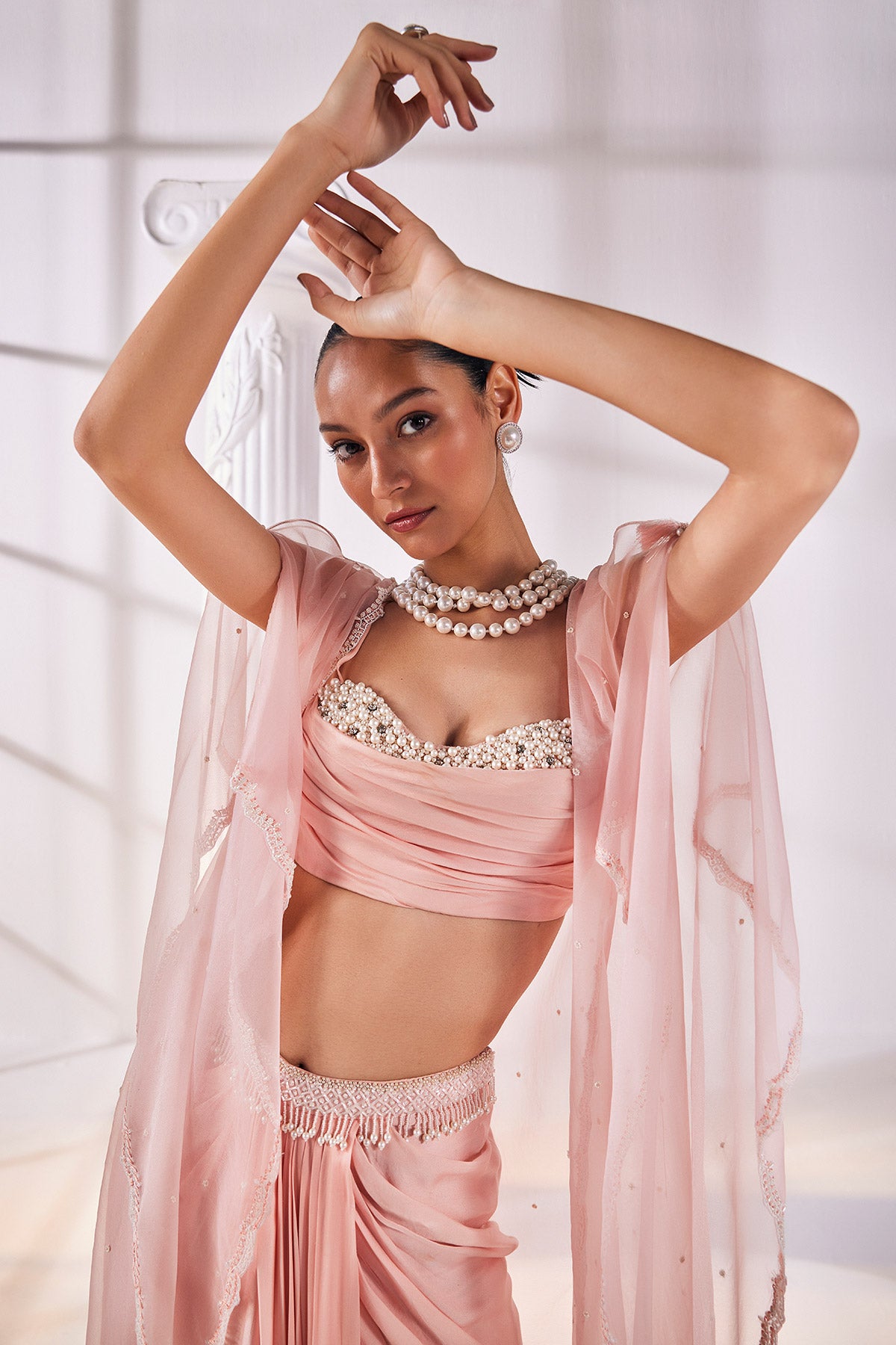 Peach Draped Skirt In Satin Georgette Paired With A Belt And A Pearl Detailed Blouse With A Soft Organza Cape.