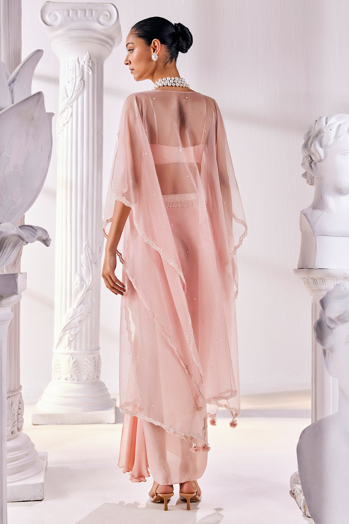 Peach Draped Skirt In Satin Georgette Paired With A Belt And A Pearl Detailed Blouse With A Soft Organza Cape.