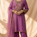 A purple three-piece salwar kameez suit set with a matching sheer dupatta, displayed on a mannequin. The kurta features intricate gold, green, and pink floral embroidery on the chest and sleeves, with gold zari borders.