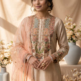 A beige three-piece traditional outfit displayed on a mannequin, featuring a long kurta with colorful floral embroidery around the neckline and cuffs, matching trousers, and a sheer light pink dupatta draped over one shoulder.