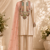 A beige three-piece traditional outfit displayed on a mannequin, featuring a long kurta with colorful floral embroidery around the neckline and cuffs, matching trousers, and a sheer light pink dupatta draped over one shoulder.