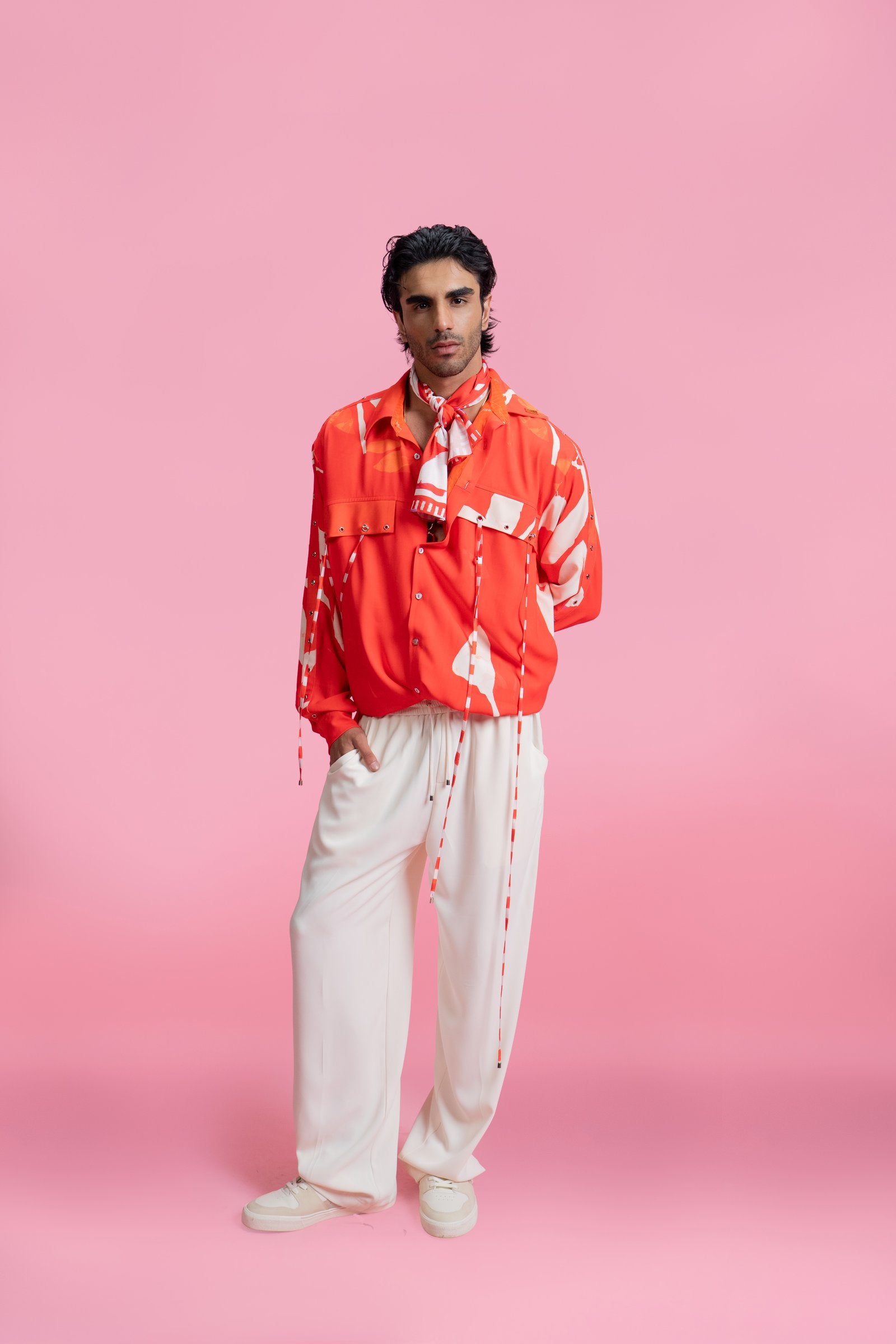 Person wearing a red jacket and white pants on a pink background resort wear by mandira wirk 
