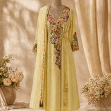 A light yellow traditional kurta set with colorful floral embroidery displayed on a mannequin. The set includes a long kurta with a V-neck, long sleeves, and a self-tie waist, paired with matching trousers.