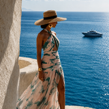 Woman wearing a blush pink and green printed halter-neck resort dress by Mandira Wirk, overlooking the blue sea.