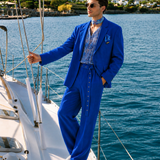 Male model wearing a cobalt blue resort wear suit with a printed shirt and neck scarf by Mandira Wirk, photographed aboard a luxury yacht.