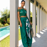 Model wearing an emerald green crop top and draped trouser resort wear set by Mandira Wirk, styled with a printed scarf at a luxury poolside villa.